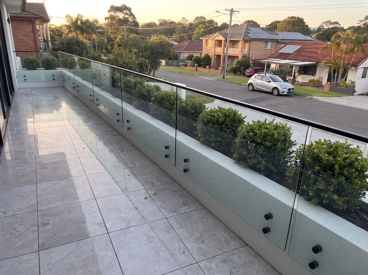 Tiled balcony with frameless glass balustrade and a long planter box of green shrubs
